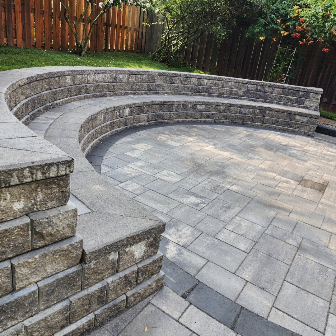 Curved retaining wall with built-in seating around a paved backyard terrace by A New Look Construction