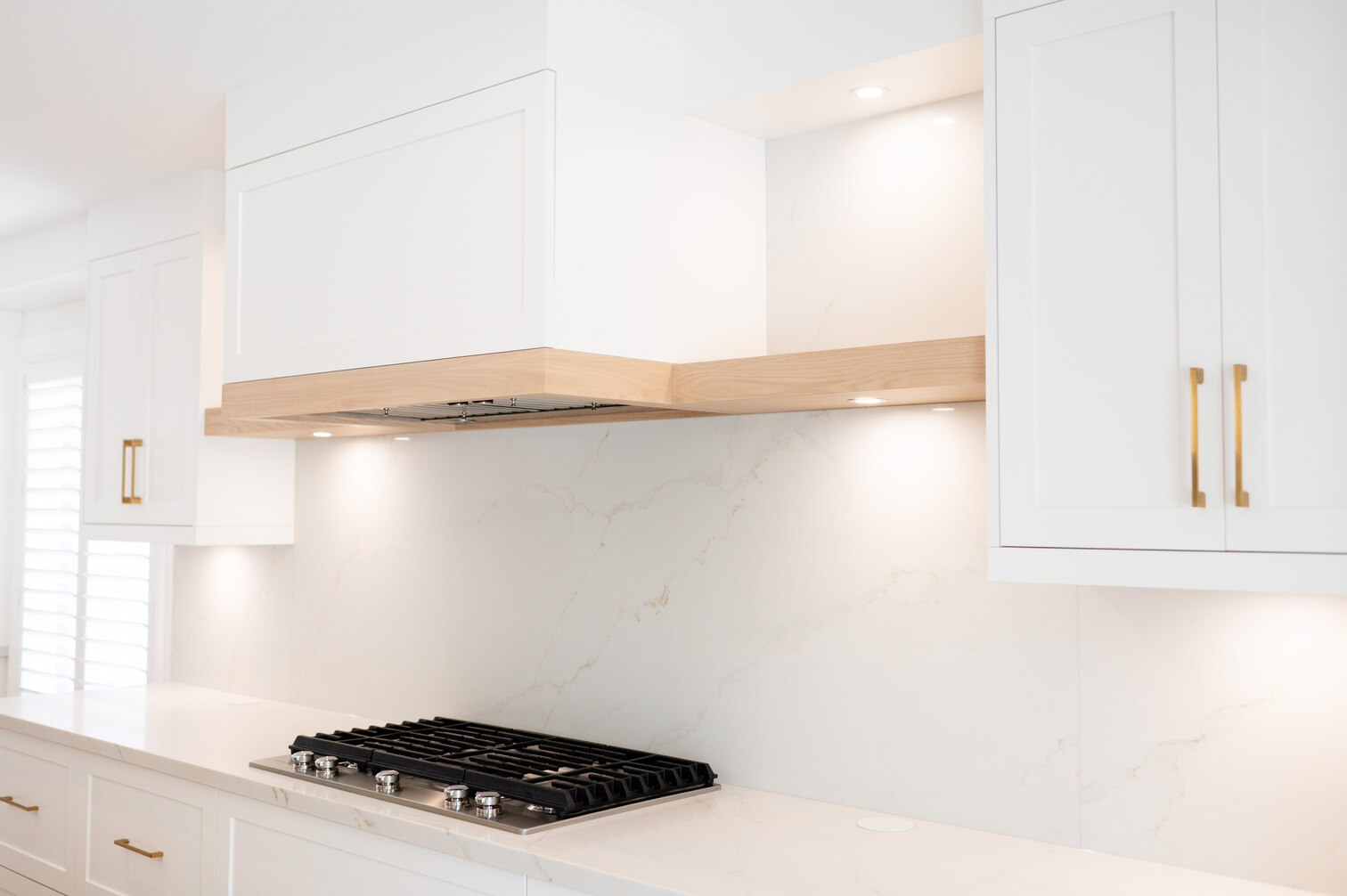 Custom range hood with white oak shelf and marble-look backsplash