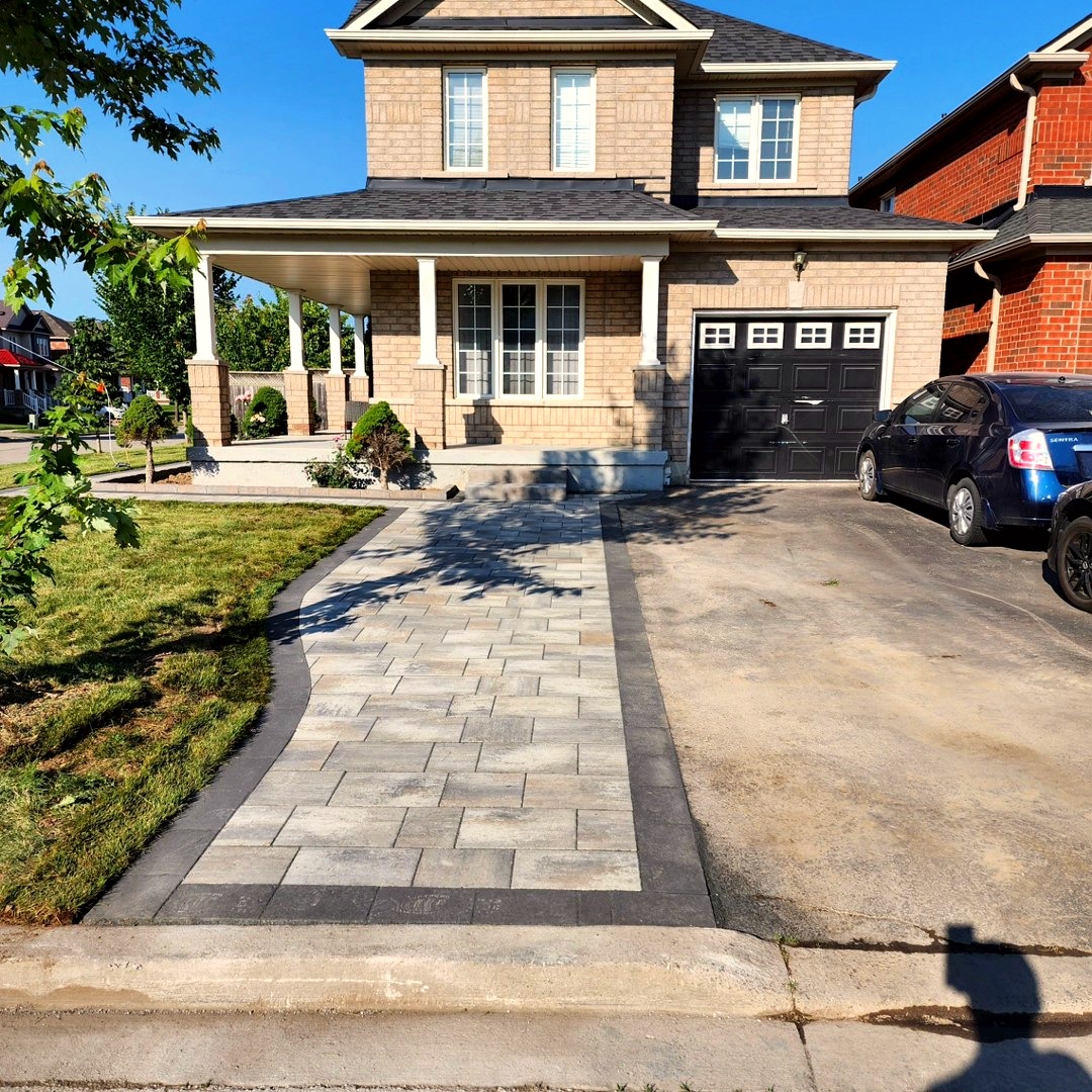 Curved grey paver walkway with charcoal border leading to a two-storey brick home
