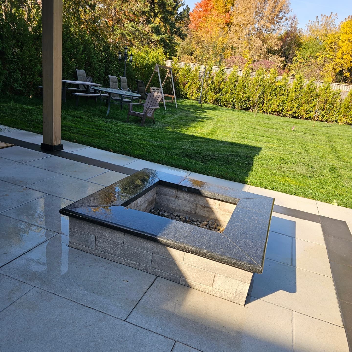 Square stone fire pit with granite cap on an interlocking patio overlooking a landscaped lawn