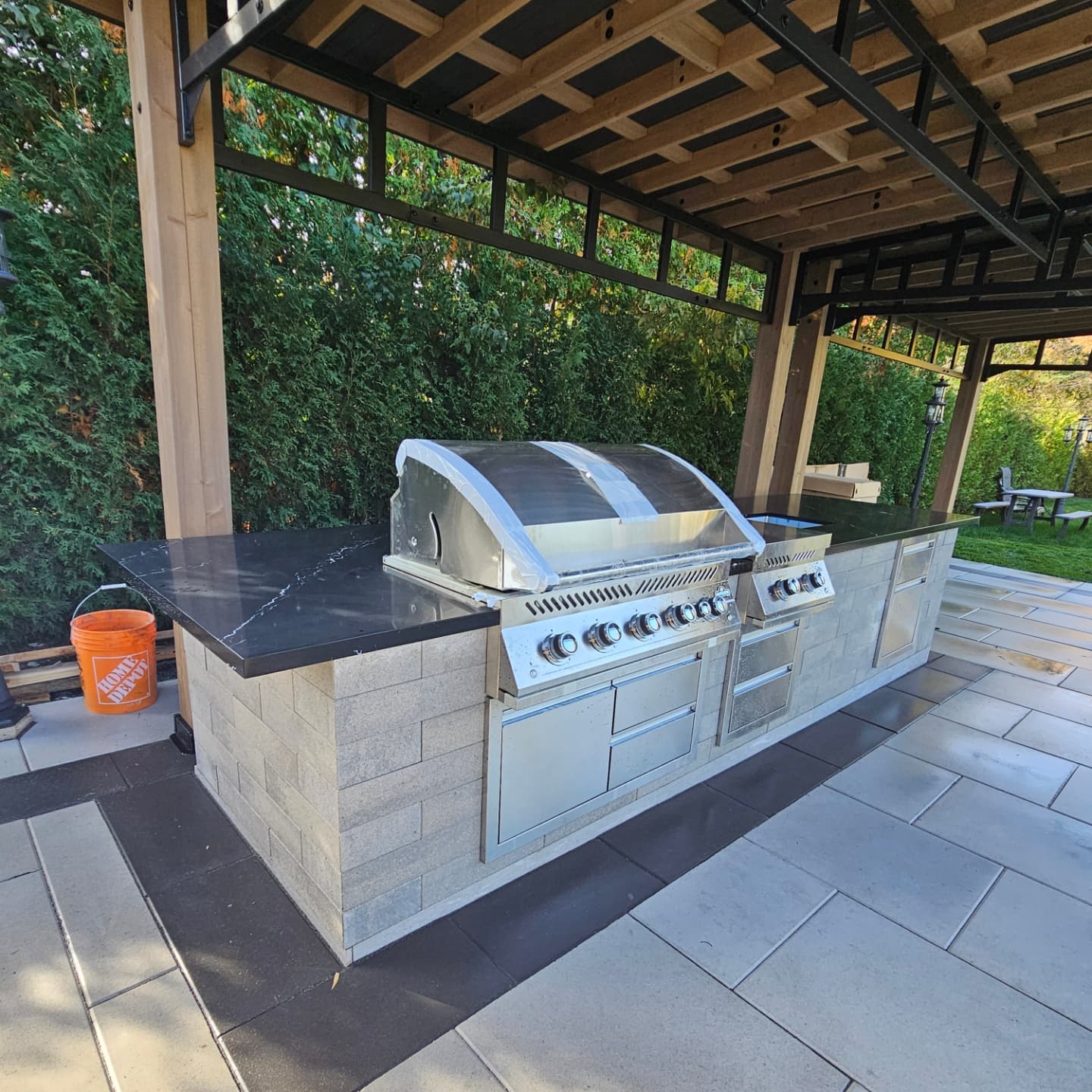 Custom outdoor kitchen with built-in grill, stone base and granite counters under timber pergola