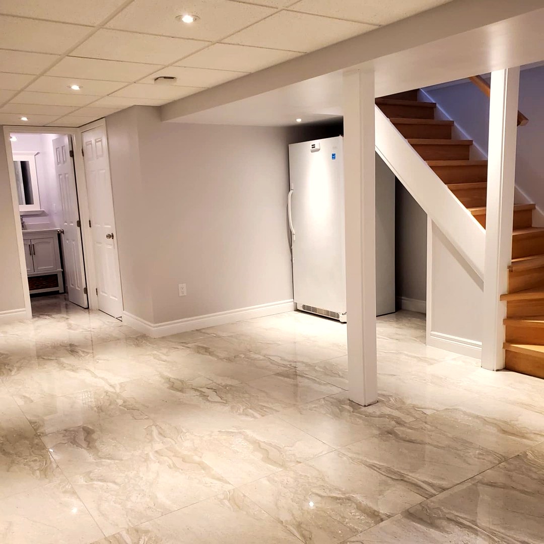 Bright finished basement rec room with glossy tile floors and open staircase